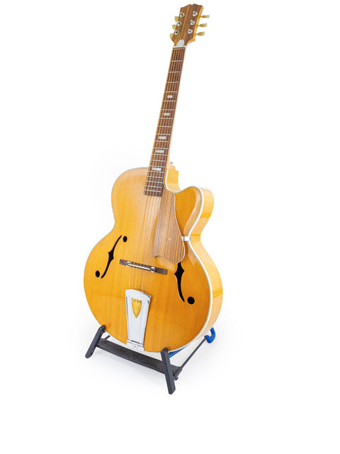 1970s Sutton Archtop guitar resting on a stand, set against a simple white backdrop.