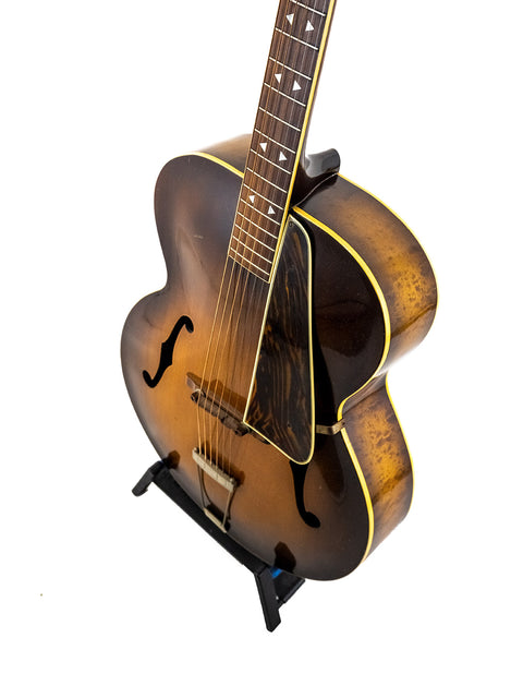 A 1940s Vintage Gibson L 7 Special guitar displayed on a stand, set against a simple white backdrop.