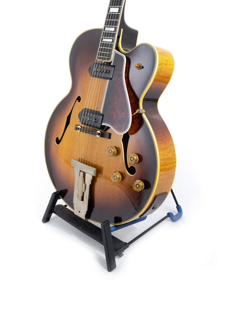 A 1955 Gibson L-5 CES guitar with Alnico pickups displayed on a stand, set against a white backdrop.