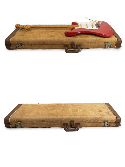 A 1957 Fender Stratocaster in Dakota Red placed atop two old cases, highlighting a blend of nostalgia and musical craftsmanship.