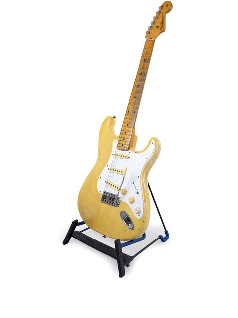 A 1959 Fender Stratocaster guitar with a blond finish and maple neck displayed on a stand, set against a white backdrop.