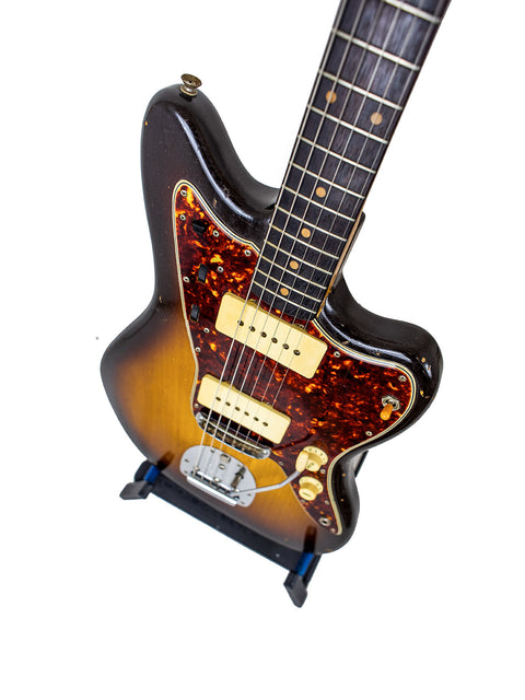 A 1960 Vintage Fender Jazzmaster guitar with a sunburst finish elegantly positioned on a stand, highlighting its craftsmanship.