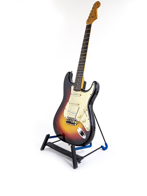 A 1964 Fiesta Red Fender L Series Stratocaster guitar elegantly positioned on a stand with a white backdrop.