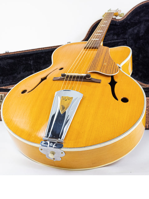 A 1970s Sutton Archtop guitar placed in its case on the floor, emphasizing its retro appeal and craftsmanship.