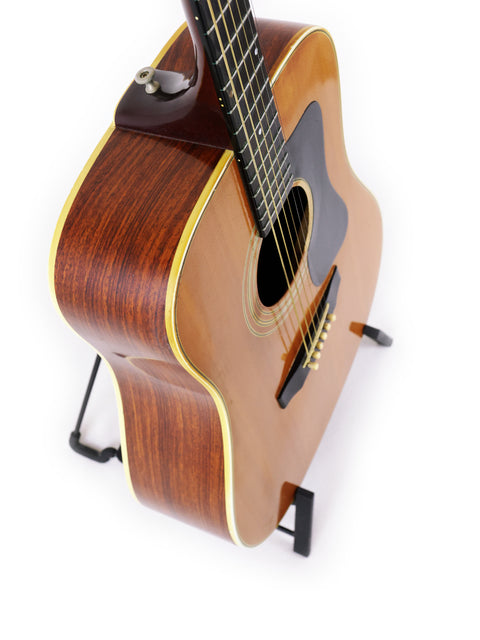 A 1974 Guild D-50 Bluegrass Special guitar elegantly positioned on a stand, set against a white background.