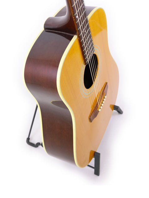 A 1989 Guild D40 guitar stands elegantly on a stand, with a stark white background emphasizing its features.