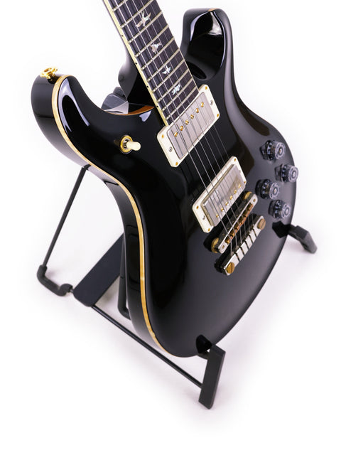 PRS McCarty 594 guitar in black, elegantly displayed on a stand with a bright white background.