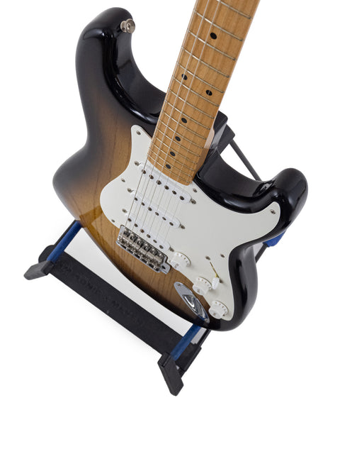 A black-bodied guitar with a brown neck rests on a stand, showcasing its elegant design and craftsmanship.