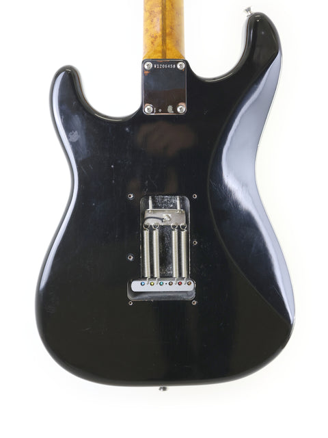 A black electric guitar with a wooden body, specifically a Fender AVRI ‘56 Stratocaster from the USA, 2012 model.