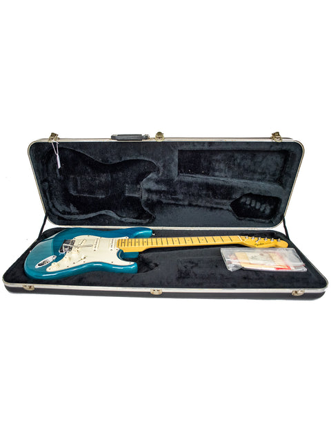 A blue Fender American Deluxe Stratocaster electric guitar resting in its case, highlighting its vibrant color and quality.