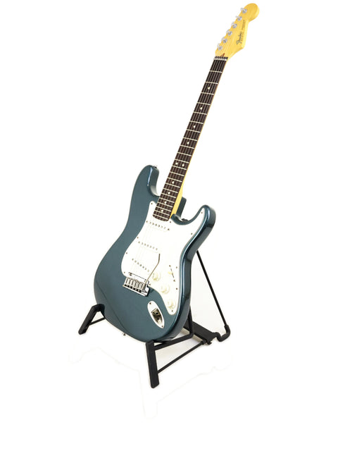 A blue Fender Strat Plus Deluxe guitar from 1989 displayed on a stand against a clean white background.