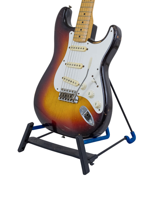 A blue background highlights a vintage 1958 Fender Stratocaster guitar on a stand.