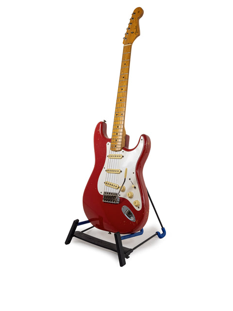 A classic 1957 Fender Stratocaster, refinished in Dakota Red, showcased on a stand with a clean white backdrop.