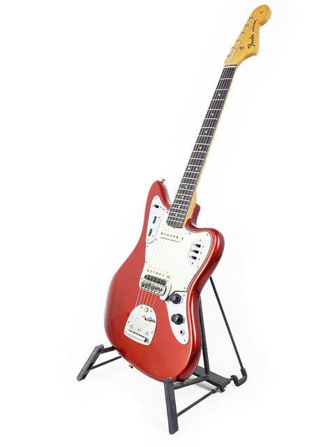 A classic red Fender Jaguar guitar from 1964, elegantly positioned on a stand with a minimalist white background.