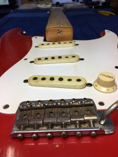 A close-up of a red 1957 Fender Stratocaster guitar, emphasizing its white pickups and vintage Dakota Red refinishing.