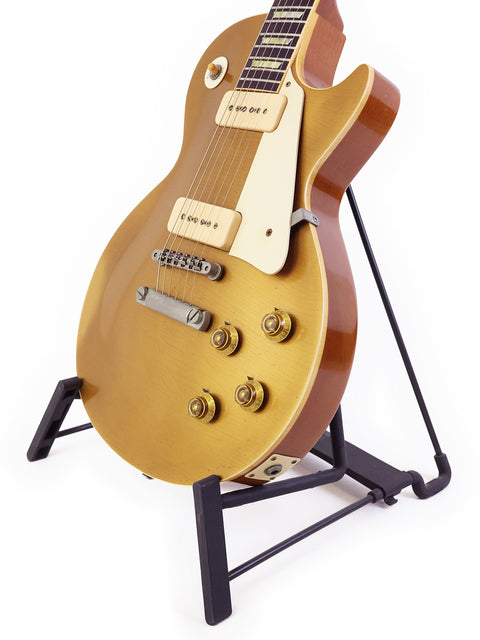 A gold Gibson Les Paul guitar on a stand, set against a clean white background, showcasing its elegant design and upgrades.