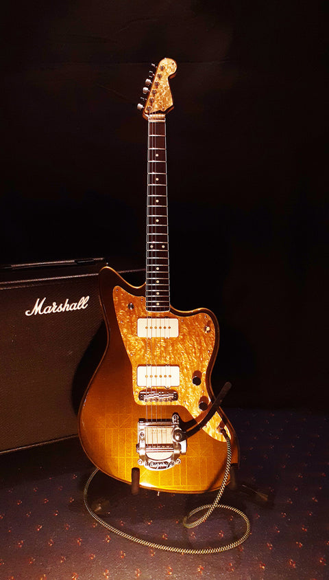 A gold guitar with a sleek black amp and case, representing the Zachary & Mercer Mastermind “Deluxe” Offset from Aust 2021.