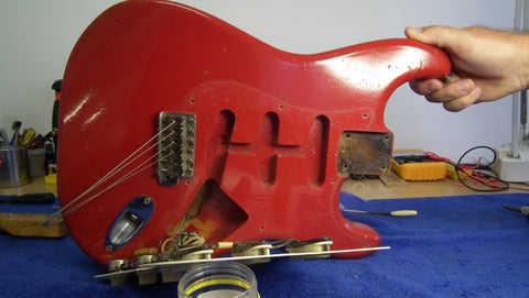 A hand holds a vintage 1957 Fender Stratocaster guitar, distinguished by its eye-catching Dakota Red color.