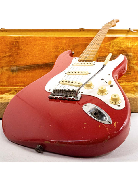 A red 1957 Fender Stratocaster guitar in Dakota Red finish, accompanied by a wooden case, highlighting its vintage appeal.