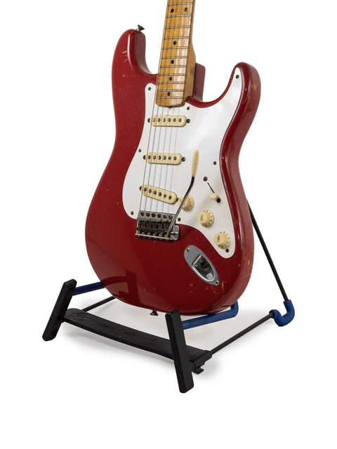 A red 1957 Fender Stratocaster guitar on a stand, featuring a black base, showcasing its vintage Dakota Red finish.