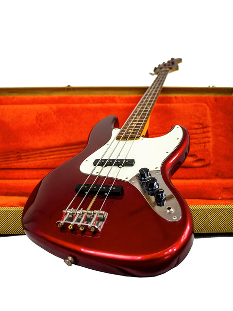 A red Fender Custom Shop ‘62 Jazz Bass Reissue guitar nestled in an orange case, showcasing its vibrant color and design.