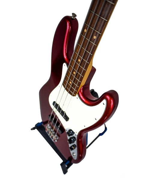 A red Fender Custom Shop ‘62 Jazz Bass Reissue guitar resting on a stand, highlighting its classic design and bold color.