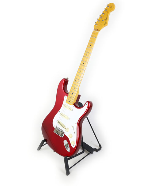 A red Fender Vintage Hot Rod ‘57 Stratocaster guitar on a stand against a clean white background.