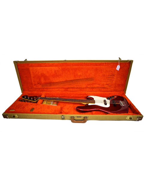 A red and black Fender Custom Shop ‘62 Jazz Bass Reissue guitar nestled in an orange case, showcasing its vibrant colors.