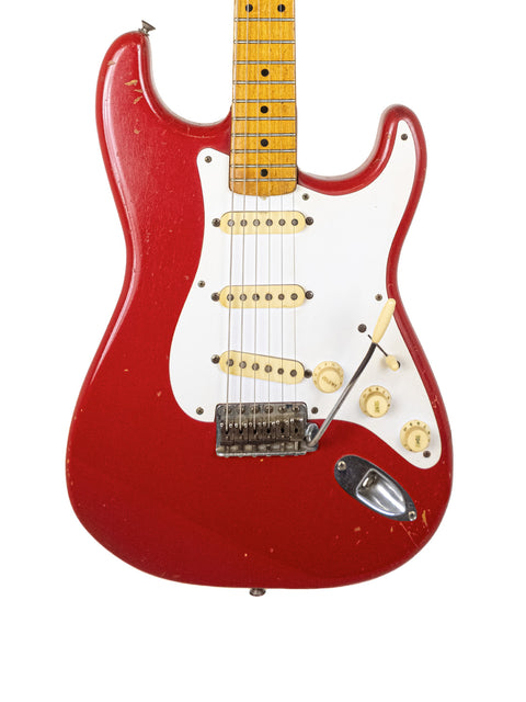 A red electric guitar, specifically a 1957 Fender Stratocaster, featuring a white pickguard and a vintage Dakota Red finish.