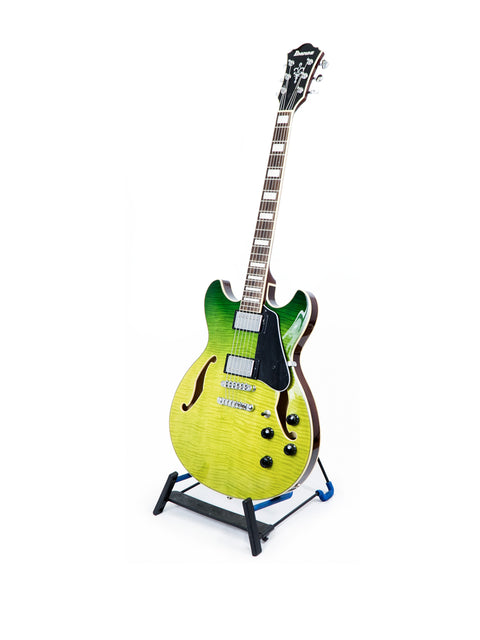 A striking green and yellow Ibanez Artcore AS73 FM guitar rests on a stand, highlighting its unique semi-hollow body style.