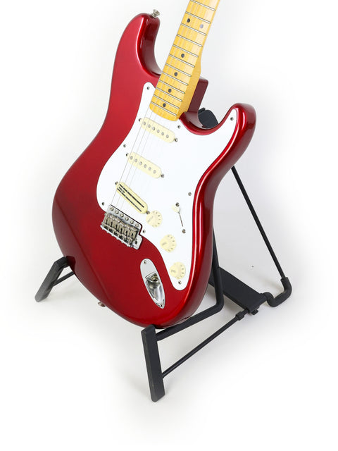 A striking red Fender Vintage Hot Rod ‘57 Stratocaster guitar displayed on a stand with a plain white backdrop.