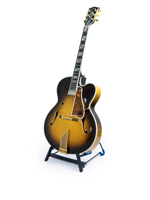 A stunning Gibson Custom Shop Le Grand Archtop guitar on a stand, highlighted by a simple white background.