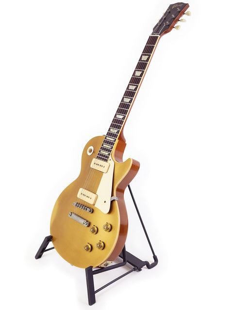 A stunning gold Gibson Les Paul guitar displayed on a stand, featuring a white backdrop that highlights its classic beauty.
