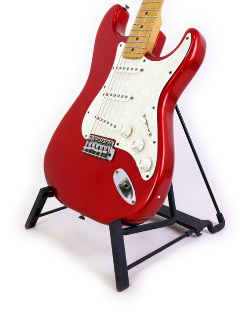 A vibrant red Fender Stratocaster guitar from 1979 displayed on a stand, contrasting beautifully with a white backdrop.