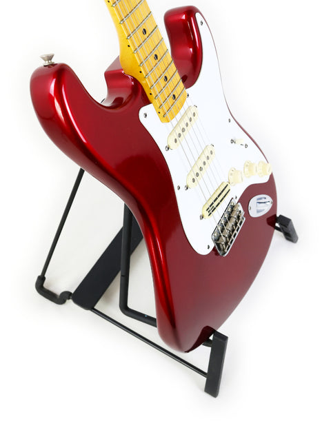 A vibrant red Fender Vintage Hot Rod ‘57 Stratocaster guitar resting on a stand, set against a plain white background.