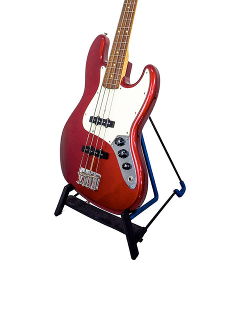 A vibrant red bass guitar, the Fender Custom Shop ‘62 Jazz Bass Reissue, positioned on a stylish black stand.
