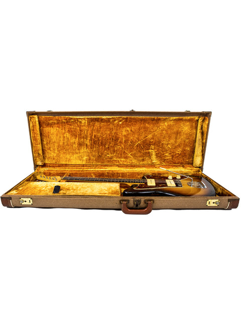 A vintage 1960 USA Fender Jazzmaster guitar in a brown case, with a gun placed inside the case.