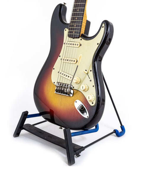 A vintage 1964 Fender Stratocaster in Fiesta Red positioned on a blue guitar stand.
