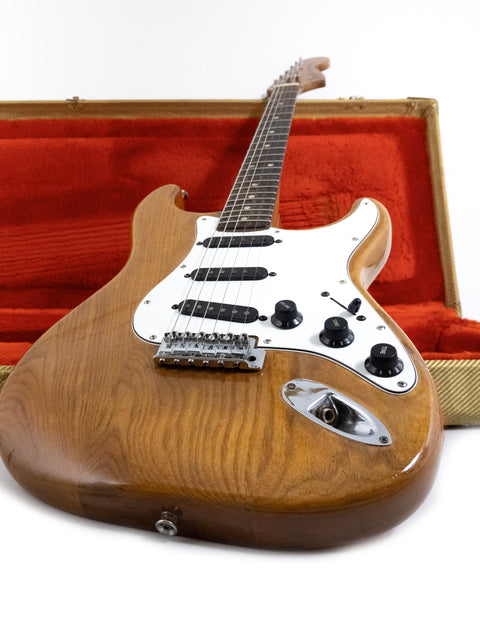 A vintage 1979 Fender Stratocaster resting in a wooden case, highlighted by a bright red outer shell.