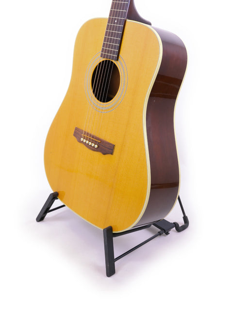 A vintage 1989 Guild D40 guitar rests on a stand, showcased against a bright white backdrop.