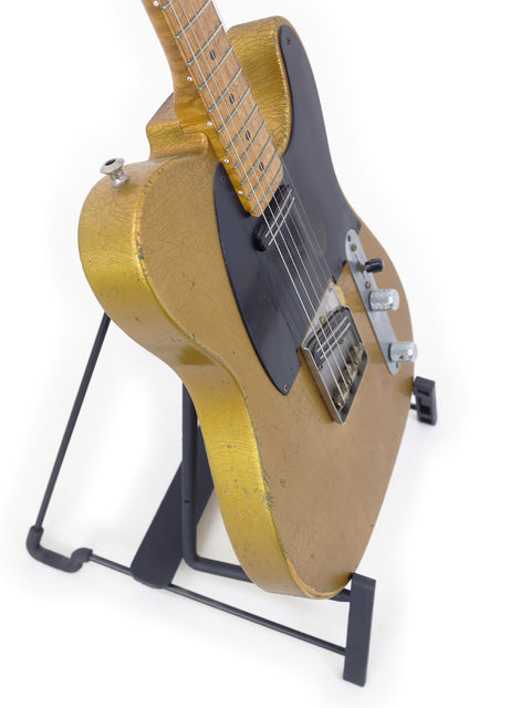 A worn gold-and-black electric guitar resting on a stand, isolated on white background.