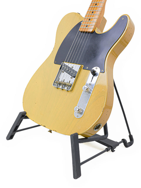 A yellow guitar on a stand, the Fender Master Built Jason Smith Esquire, with a black strap, crafted in the USA, 2018.