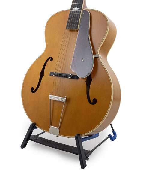 An Epiphone Masterbilt De Luxe F-Hole Archtop guitar from 2016 resting on a stand, adorned with a strap.