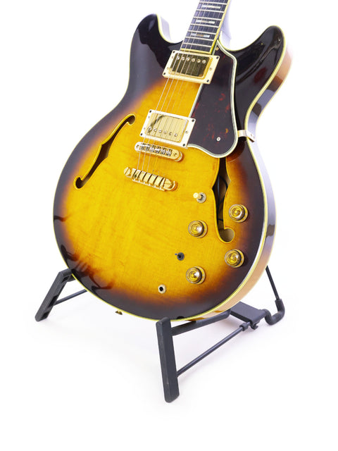 An Ibanez Artist AS200 guitar from 1981 displayed on a stand, set against a minimalist white backdrop.