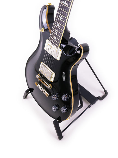 Black PRS McCarty 594 guitar on a stand, highlighted by a stark white background for a striking visual effect.