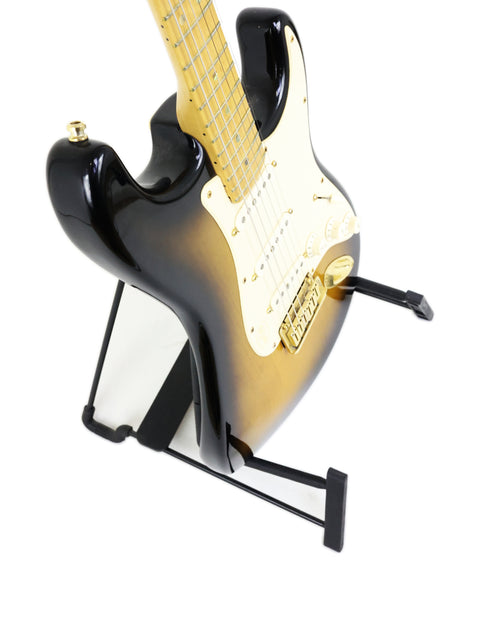 Black and gold electric guitar on a stand, isolated on white background.