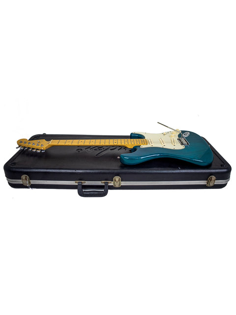 Blue electric guitar, a Fender American Deluxe Stratocaster, resting in its case on a bright white background.