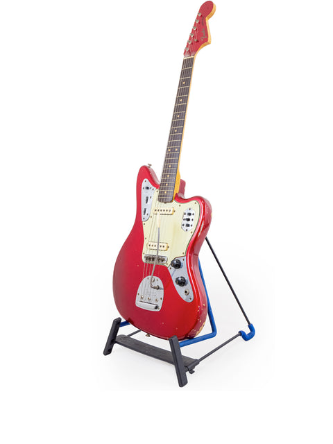 Candy Apple Red 1964 Fender Jaguar guitar displayed on a stand with a blue base, highlighting its vintage charm.