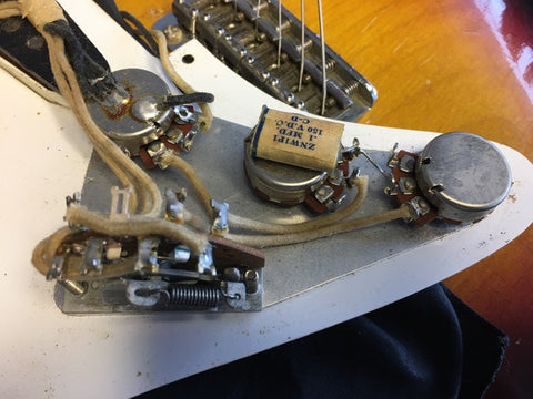 Close-up of a vintage 1958 Fender Stratocaster guitar with a pickup and wires, emphasizing its iconic style and history.