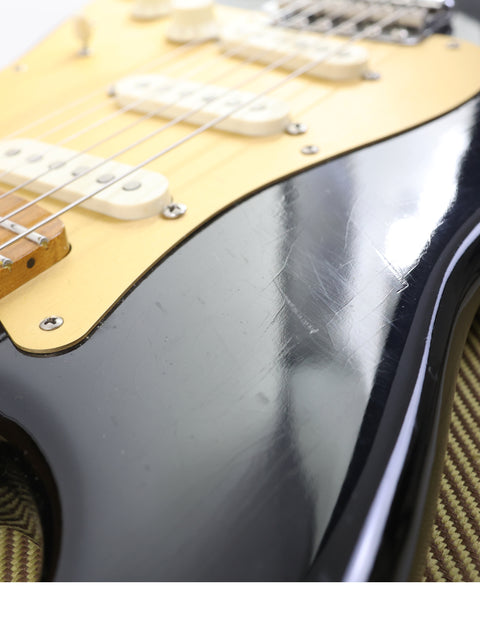Detailed view of a black and gold Fender AVRI ‘56 Stratocaster guitar, highlighting its stunning finish and classic features.